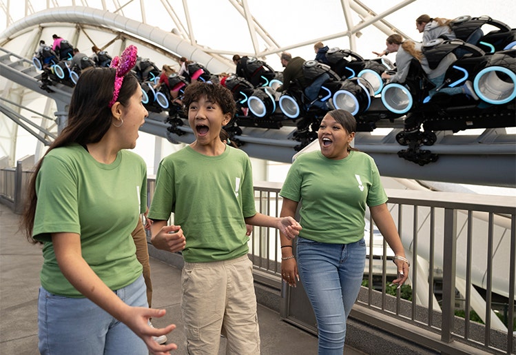 Students walking as Guests ride Tron Lightcycle Run nearby